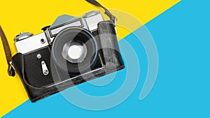 Vintage film photo camera on a colorful blue and yellow background, top view
