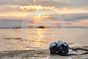 Vintage film photo camera. Front view, close up photo. Against the background of the sea. Beautiful sunset, waves and landscape