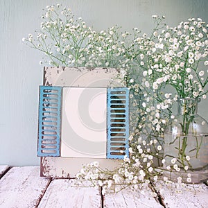 Vintage filtered image of old wooden frame next to white flowers on wooden table. template, ready to put photography