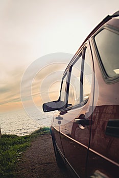 Vintage-filtered photo from the side of a 1990s classic red sports car with beautiful view of sunset by the sea