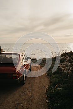 Vintage-filtered photo from up high on the right side of a 1990s classic red sports car with beautiful view of sunset by the sea