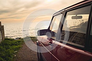 Vintage-filtered photo from the upperside of a 1990s classic red sports car with beautiful view of sunset by the sea