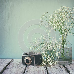 Vintage filtered and toned image of fresh white flowers and old camera over wooden table.