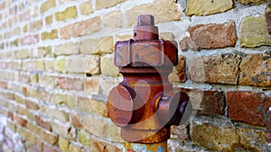 Vintage fire hydrant of red colour with rusty valve by wall
