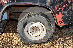 Vintage flat tire on retro truck parked on wood chips