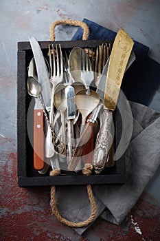 Vintage forks, spoons and knives in a dark old wooden box on a gray concrete or stone background. Selective focus.Top view. Copy