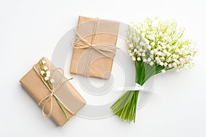 Vintage gifts wrapped kraft paper and bouquet of flowers lily of the valley on white table from above. Wedding or anniversary