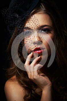 Vintage glam. A dramatically made-up young woman wearing a stylish hat with a netted veil.