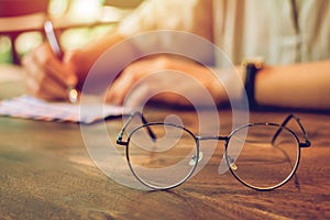 Vintage glasses,on wood table ,Man holding a pen  writing the  letter paper with sunset background. Copy space for you text