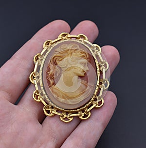 Vintage gold cameo brooch on a woman's hand, old retro jewelry