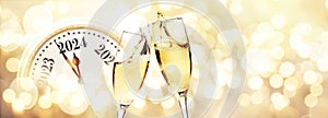 Vintage gold clock strikes New Year 2024 with glasses of champagne on a beige background with bokeh lights. New Year 2024 and