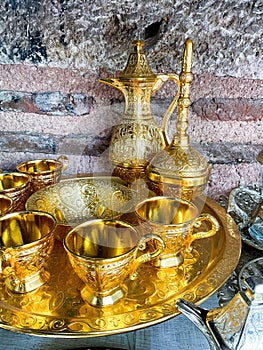 Vintage golden tea set with intricate designs on tray against rustic stone wall. Traditional ornate metalware concept photo
