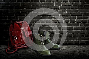 Vintage green boot and red backpack made of genuine leather on a background of a dark brick wall