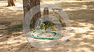 Vintage Green Water Hose and Red Valve in the Garden under Big Tree with Old Rustic Wooden Stool