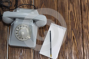 Vintage grey phone, writing pad on wooden background close-up, top view