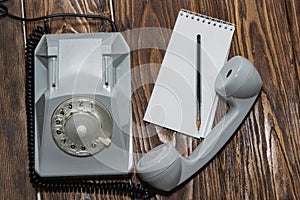 Vintage grey phone, writing pad on wooden background close-up, top view