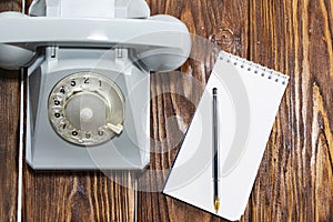 Vintage grey phone, writing pad on wooden background close-up, top view