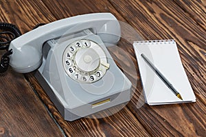 Vintage grey phone, writing pad on wooden background close-up, top view