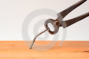 Vintage grungy forged pincers pull bent big nail out of the board