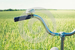 Vintage handlebar with bell on bicycle. Summer day for trip. View of wheat field. Outdoor. Closeup.