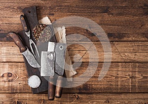 Vintage hatchets for meat on wooden chopping board with salt and pepper on wooden table background with linen towel and fork and