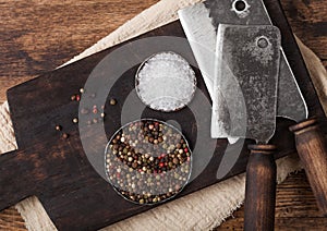 Vintage hatchets for meat on wooden chopping board with salt and pepper on wooden table background. Macro