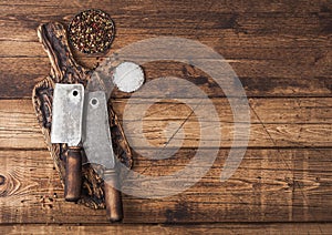 Vintage hatchets for meat on wooden chopping board with salt and pepper on wooden table background. Space for text