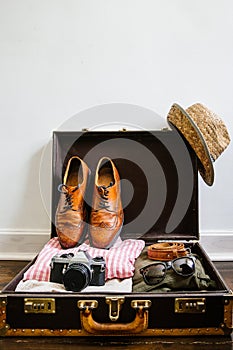 Vintage hipster clothes, shoes, hat, smartphone, accessories packed in suitcase on wooden floor. Travel concept. Empty space for