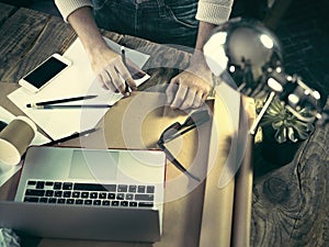 Vintage hipster wooden desktop top view, male hands using a laptop and holding a pencil