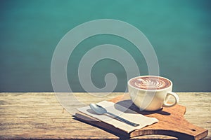 Vintage of hot coffee cup cappuccino art, spoon, tissue, chopping board on wooden table with copy space