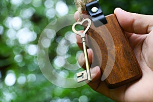 Vintage house key with wooden home keyring on hand with blur green garden background, property concept, copy space