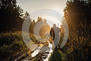 Vintage hunter walks the forest road. Rifle Hunter Silhouetted in Beautiful Sunset or Sunrise. Hunter aiming rifle in