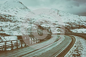 Vintage image of winter road and bridge between Lofoten Islands, moody dramatic landscape