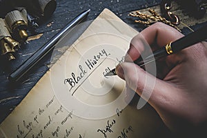 Vintage-inspired scene of a hand penning the words & x27;Black History& x27; on aged paper with ink and quill nearby photo