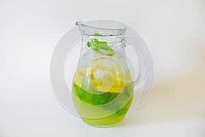 Vintage jug with refreshing non alcoholic mojito drink with lemon slices, mint leaves and ice. Studio shot of iced lemonade