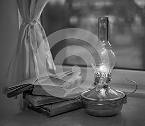 Vintage kerosene lamp with fire on a blurred background of the window and curtains with a book and glasses