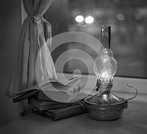 Vintage kerosene lamp with fire on a blurred background of the window and curtains with a book and glasses