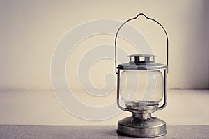 Vintage kerosene oil lantern lamp standing on cement floor with white wall background.