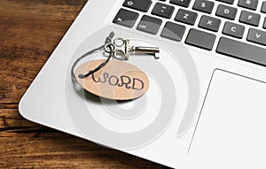 Vintage key with tag and laptop on wooden table, closeup. Keyword concept