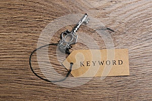 Vintage key and tag wIth word KEYWORD on wooden table, top view