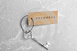 Vintage key and tag wIth word KEYWORDS on light grey table, top view