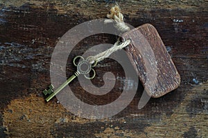 Vintage key with wooden home keyring hanging on old wood plank with blur green garden background, copy space