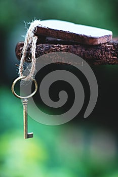 Vintage key with wooden home keyring hanging on old wood plank with blur green garden background, copy space