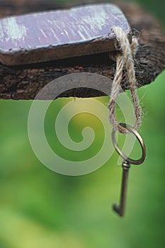 Vintage key with wooden home keyring hanging on old wood plank with blur green garden background, copy space