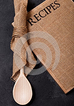 Vintage kitchen wooden utensils with linen recipes board on black stone table background. Top view.