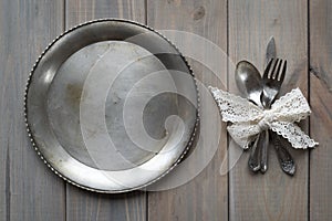 Vintage knife, spoon and fork on a metal plate on a gray wooden background.