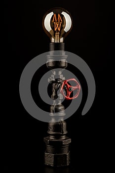 Vintage lamp made from steel water pipe fittings with filament bulb and valve switch, on black background