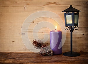 Vintage Lantern with burning Candle and pine cones on wooden table. filtered image