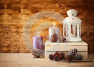 Vintage Lantern with burning Candle and pine cones on wooden table. filtered image