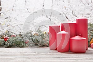 Vintage lantern red candles with Christmas fir tree garland on wooden board on window sill over nature snowing tree park backgroun